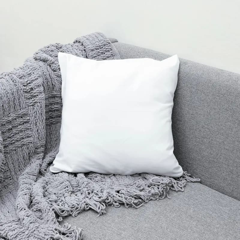 Manta tejida gris sobre un sofá con un cojín blanco